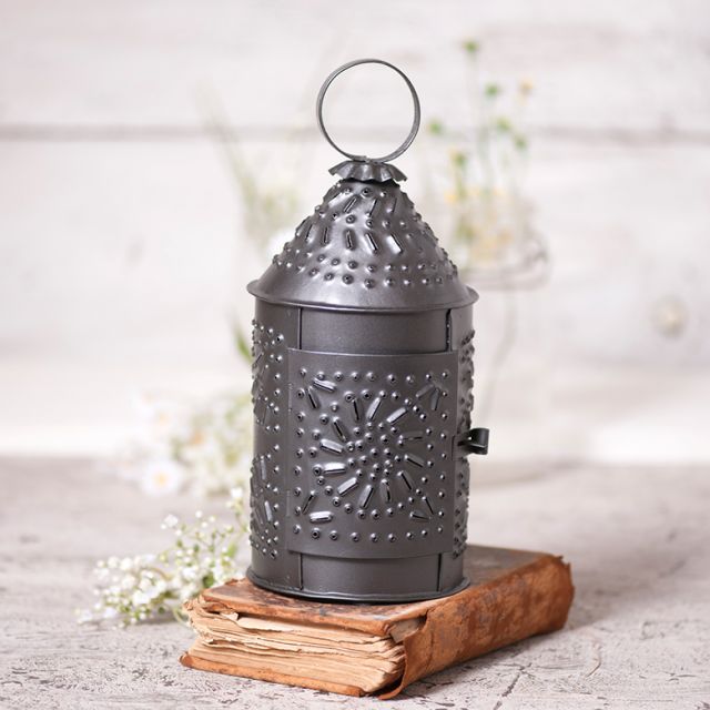 Punched tin Paul Revere lantern sitting on top of a book with artificial flowers beside it