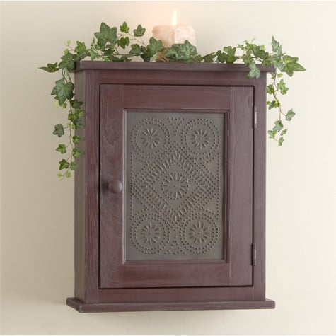 Punched tin panel displayed in a burgundy cupboard with candle and artificial greenery on top